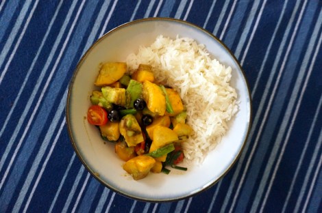 An overhead shot of a bowl of colorful summer squash saute; the saute sits in the lower left, with a mound of rice in the upper right