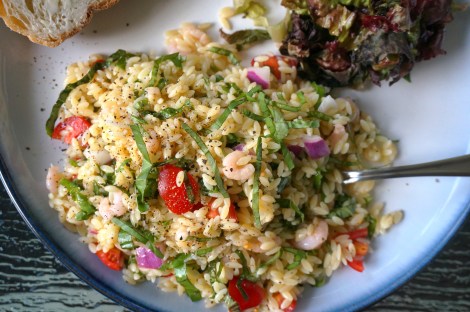 Orzo salad with shrimp and basil, plated, with a fork buried in it and a bit of bread and a green salad visible