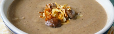 A bowl of mushroom bisque, in close-up filling almost the whole frame, with a small cluster of mushroom quarters and fried shallots floating in the middle of the bowl.
