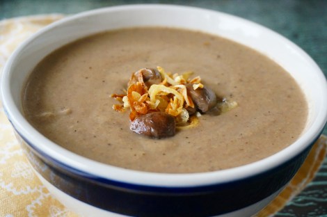 A bowl of mushroom bisque, in close-up filling almost the whole frame, with a small cluster of mushroom quarters and fried shallots floating in the middle of the bowl.