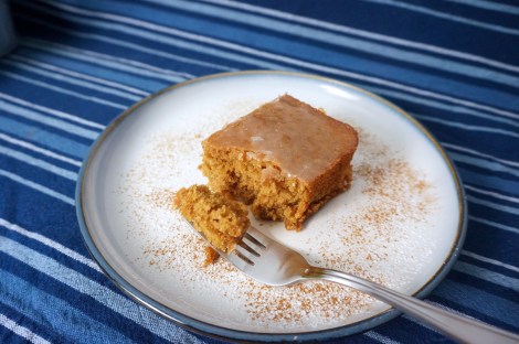 A square of No-Cola cake sits on a plate dusted with cinnamon and powdered sugar. A forkful has been taken off, and sits on the fork in the foreground.
