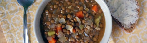 A bowl of basic lentil soup sits on a yellow napkin, along with a shiny spoon and a piece of thickly buttered bread
